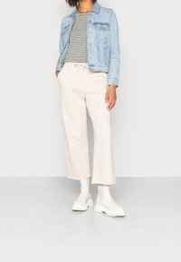 Chaqueta de mezclilla azul clara sobre una camiseta a rayas, combinada con pantalones anchos color crema y botines blancos gruesos. Diseño sencillo, ajuste relajado.