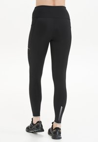 Zwarte leggings met een hoge tailleband, zijzak en reflecterende strips aan de onderkant van het been. Gemaakt van rekbaar materiaal voor comfort.