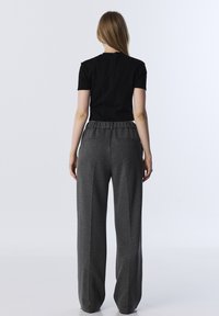 Černý přiléhavý top s krátkými rukávy, skombinovaný s volnými šedými kalhotami s elastickým pasem a postranními kapsami.