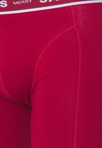 Unterhose mit rotem Bund, die durch eine glatte Textur, eine enge Passform und kontrastierende weiße Nähte an den Nähten besticht.