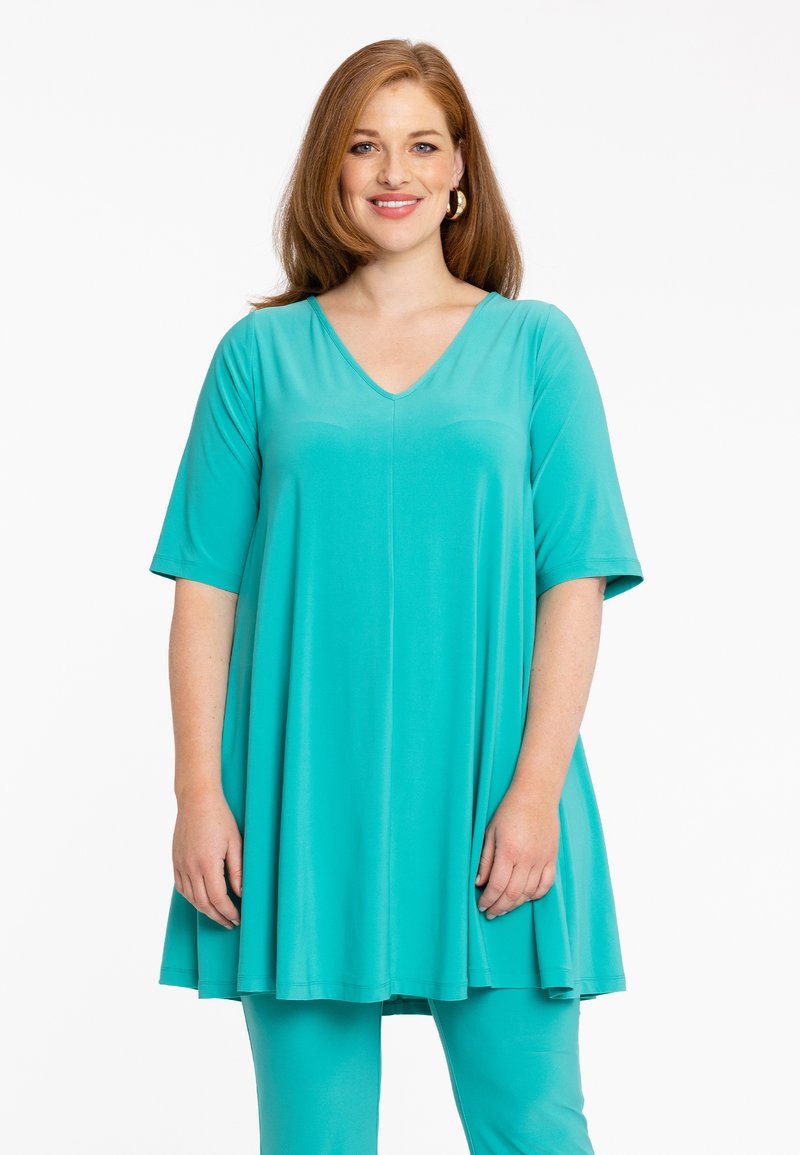 Turquoise tuniek met een V-hals en korte mouwen, voorzien van een losse pasvorm en een zachte stof. Complementaire leggings maken de outfit compleet.