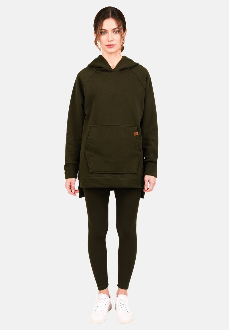 Oliwkowa tunika z kapturem z przednią kieszenią, teksturowaną tkaniną i luźnym krojem, w zestawie z dopasowanymi legginsami i białymi tenisówkami.