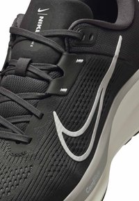 Primer plano de una zapatilla de running negra de Nike con el logo de swoosh blanco, parte superior de malla texturada, cordones negros y suela blanca ComfiRide.