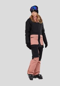 Skidragt i sort og pink stof med lynlås foran, store lommer og vandtæt materiale. Inkluderer handsker og skistøvler til vintersport.