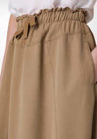 Falda caqui con cintura elástica y detalle de lazo. Presenta bolsillos laterales y una tela suave y ligera con un corte relajado.