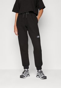 Haut court en tissu gaufré noir et pantalon de jogging noir avec taille élastique. Présentant un petit logo blanc sur la jambe du pantalon.