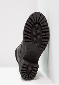 Semelle en caoutchouc noir à crampons profonds, avec des motifs circulaires et en croix. Tige en cuir noir lisse, design minimaliste. Taille 37.