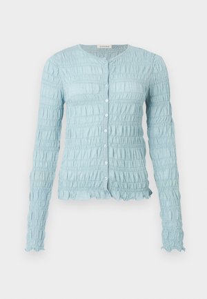 Cardigan bleu clair à manches longues avec une texture smockée, encolure ronde, boutonnage sur le devant, et bords à volants sur les manches et l'ourlet.