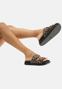 Sandali a slide con stampa leopardata, caratterizzati da una parte superiore testurizzata, dettagli con doppia fibbia e una spessa suola in gomma nera con motivo antiscivolo.