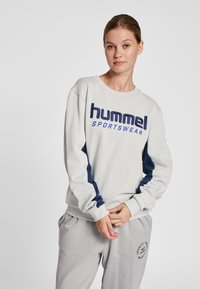 Jasnoszara bluza z granatowymi akcentami, z okrągłym dekoltem i logo "hummel SPORTSWEAR" w kolorze granatowym. Miękki materiał z ściągaczami na mankietach.