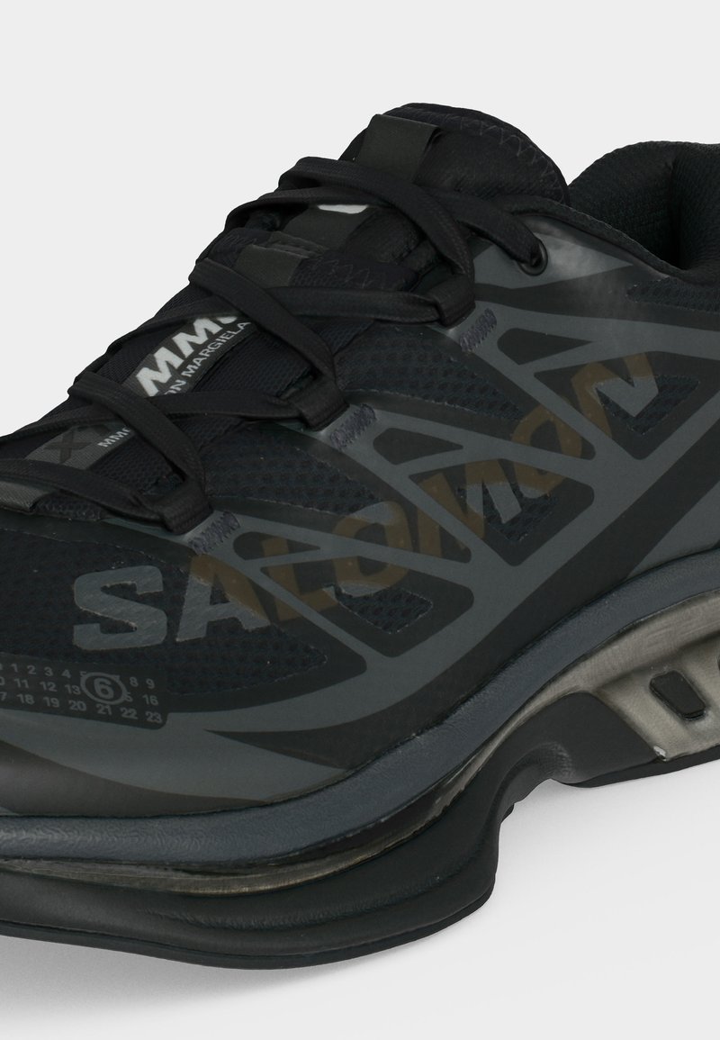Black and gray sports sneaker with mesh upper, thick cushioned sole, black laces, and "MM6 Maison Margiela" branding on the tongue and side.