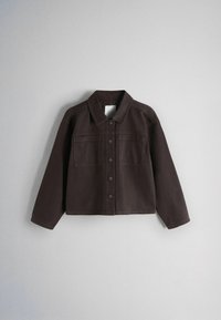 Veste marron foncé à boutons avec col et deux poches poitrine, manches longues, présentée sur un fond clair uni.