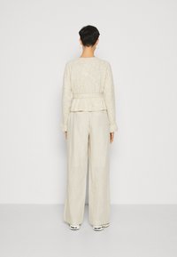 Beige textured sweater with a peplum waist paired with loose, light beige linen trousers and white sneakers. Visible seams and cuffs.