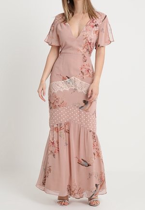 Longue robe rose blush ornée de motifs floraux et d'accents en dentelle. Tissu fluide avec un corsage ajusté, un col en V et une jupe évasée à pois.