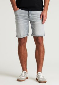 Shorts de denim azul claro con dobladillos enrollados, que cuentan con bolsillos laterales y un ajuste clásico. Combinados con zapatillas grises y blancas.