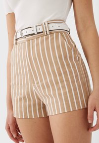 Pantaloni shorts a vita alta a righe in beige e bianco, realizzati in un tessuto dalla superficie liscia. Presentano una cintura bianca con una fibbia argento.