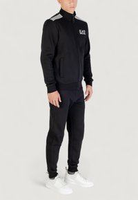 Chándal deportivo negro con chaqueta con cremallera y pantalones a juego. Presenta un logo blanco, acentos estriados en los hombros y dobladillos ajustados.