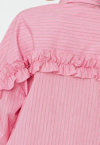 Tissu de chemise rose avec fines rayures verticales et horizontales, présentant un détail froncé horizontal sur le haut du dos et les manches.