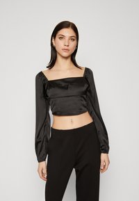 Crni satenski crop top s kvadratnim izrezom, napuhanim dugim rukavima i nabranim detaljima. Uparen s crnim hlačama visokog struka.