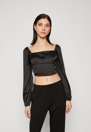 Crni satenski crop top s kvadratnim izrezom, napuhanim dugim rukavima i nabranim detaljima. Uparen s crnim hlačama visokog struka.