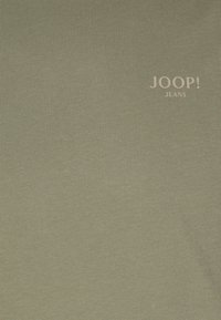 Olive green cotton t-shirt featuring a smooth texture and a subtle "JOOP! JEANS" logo in light beige. Simple design, no additional patterns.