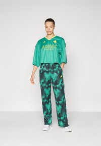 Green cropped jersey with yellow accents and "ADIDAS" logo, paired with green patterned joggers featuring side stripes and an elastic waistband.