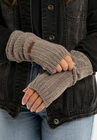 Vingerloze gebreide handschoenen in lichtgrijs, met ribstructuur, een leren merklabel en een aansluitend ontwerp, gedragen over een spijkerjack.