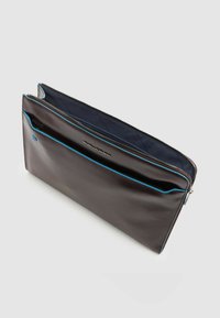 Funda para portátil de cuero marrón con acento de cremallera azul, que cuenta con un compartimento principal y un bolsillo exterior, textura suave, forma rectangular.