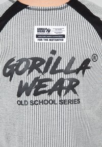 Grijs gestreept T-shirt met zwarte accenten, voorzien van een grote zwarte logo tekst "GORILLA WEAR" en een wit verzorgingslabel op de hals.