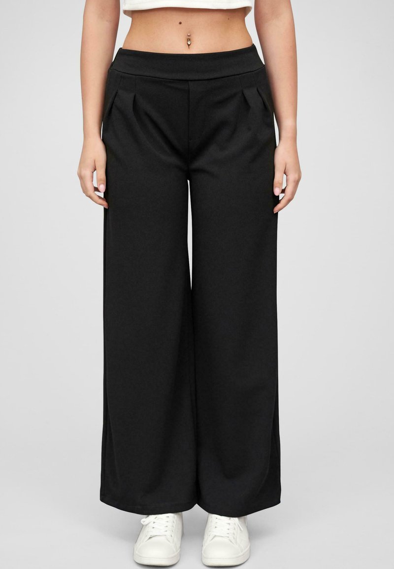 Black wide-leg pants with a smooth texture, featuring a high waistband and front pleats. Paired with white sneakers for contrast.