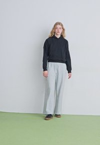 Sudadera negra con un corte holgado, pantalones de chándal grises y zapatillas negras. Diseño simple con una silueta relajada y sin patrones ni acentos visibles.