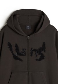 Sudadera con cremallera de color marrón oscuro, con capucha, letras abstractas en textura negra en el pecho y un bolsillo frontal tipo canguro.