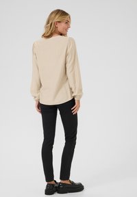 Béžová košile s dlouhým rukávem a kulatým výstřihem, s nařasenými rukávy, a černé slim-fit kalhoty spojené s černými platformovými botami.