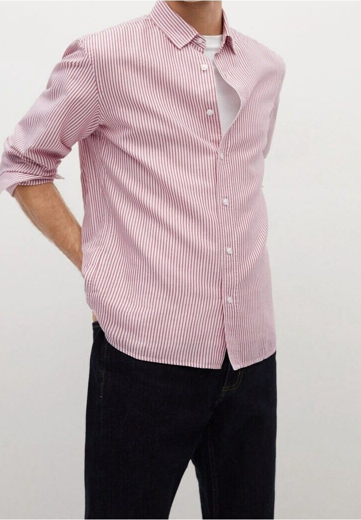 Personne portant une chemise à manches longues à rayures verticales roses et blanches avec les manches retroussées, par-dessus un sous-vêtement blanc et un pantalon noir.