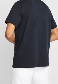 Granatowa bawełniana koszulka z krótkim rękawem, okrągłym dekoltem i luźnym fasonem. Charakteryzuje się gładką fakturą i brakiem widocznych wzorów.