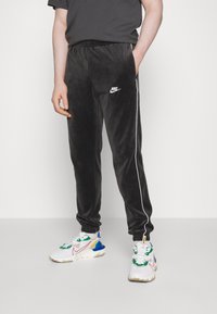 Svarta velour joggers med vita sidosträck och en liten Nike-logotyp. Matchat med färgglada Nike-sneakers med olika mönster.
