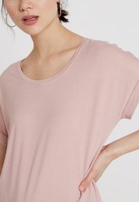 Lys rosa t-skjorte med korte ermer og rund hals, laget av et mykt materiale. Designet har en avslappet passform og en jevn tekstur.
