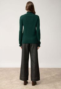 Maglione aderente a collo alto di colore verde scuro, realizzato in materiale morbido; abbinato a pantaloni in denim a gamba larga di lavaggio scuro con cuciture a contrasto.