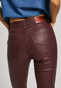 Burgundy slim-fit jeans made of stretchy material with tonal stitching and two back pockets. Leather brand patch at the waist.