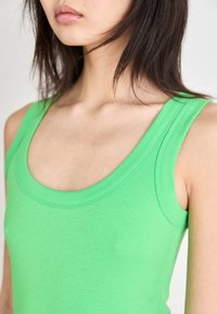 Groene tanktop met een geribbeld textuur, brede ronde halslijn en smalle schouderbandjes. De stof lijkt zacht en aansluitend.