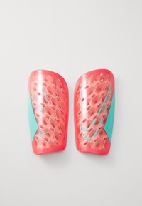 Protège-tibias de football en corail vif avec un motif en nid d'abeille, soulignés par des sections teal et un logo Nike argenté, présentant une surface texturée.