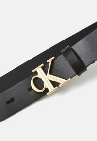 Schwarzer Ledergürtel mit einer auffälligen goldenen "CK"-Schnalle, glatter Textur und mehreren Lochstufen zur Größenanpassung.