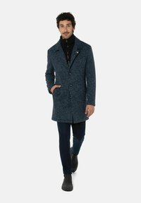 Wollen blend jas in donkerblauw met een textuurafwerking, voorzien van een kraag, voorknopen en zijzakken, gecombineerd met donkere broek en laarzen.
