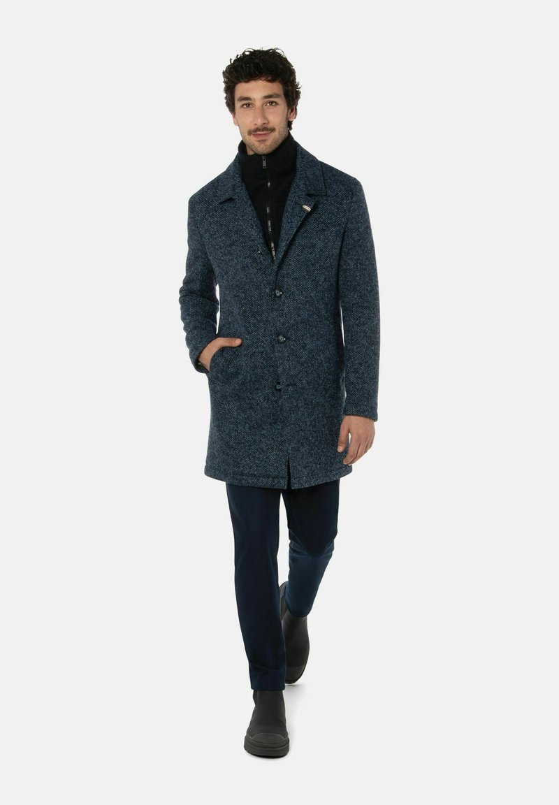 Wollen blend jas in donkerblauw met een textuurafwerking, voorzien van een kraag, voorknopen en zijzakken, gecombineerd met donkere broek en laarzen.