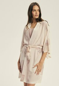 Jasnoróżowy kimono wykonany z miękkiego materiału w kwiatowe wzory w stonowanych kolorach, z szerokimi rękawami i wiązaniem w talii.