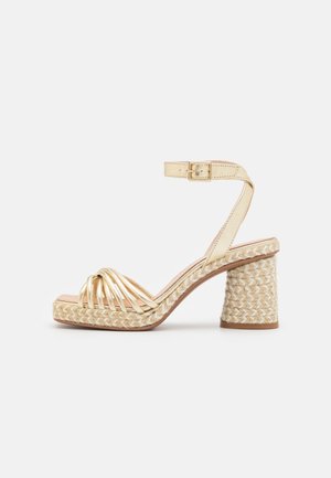Sandale beige à talon avec semelle plateforme tressée, talon bloc, brides avant dorées, et bride cheville avec petite boucle.