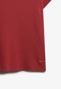 Rød bomulds T-shirt med korte ærmer, udstyret med et lille guld broderet logo i nederste venstre hjørne. Glat tekstur, afslappet pasform.