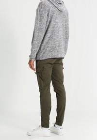 Grijze gebreide hoodie met een gestructureerde afwerking, gecombineerd met een relaxte olijfgroene cargobroek met meerdere zakken, gedragen met witte sneakers.