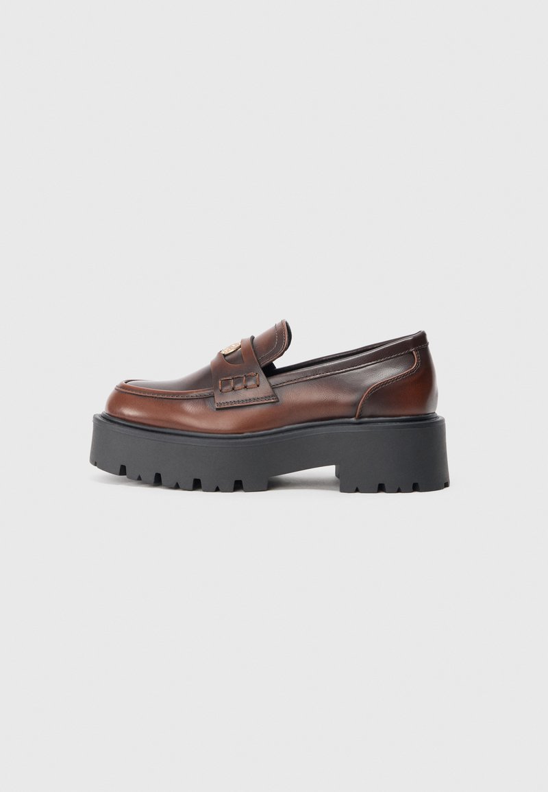 Brune skinn loafers med en kraftig svart såle, med en frontreim og subtile sømdetaljer. Flat profil og rund tådesign.