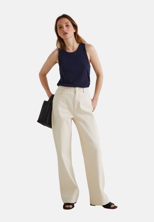 Débardeur côtelé marine associé à un pantalon large crème. Le mannequin tient un sac à main noir, porte des sandales noires. Design simple et épuré.